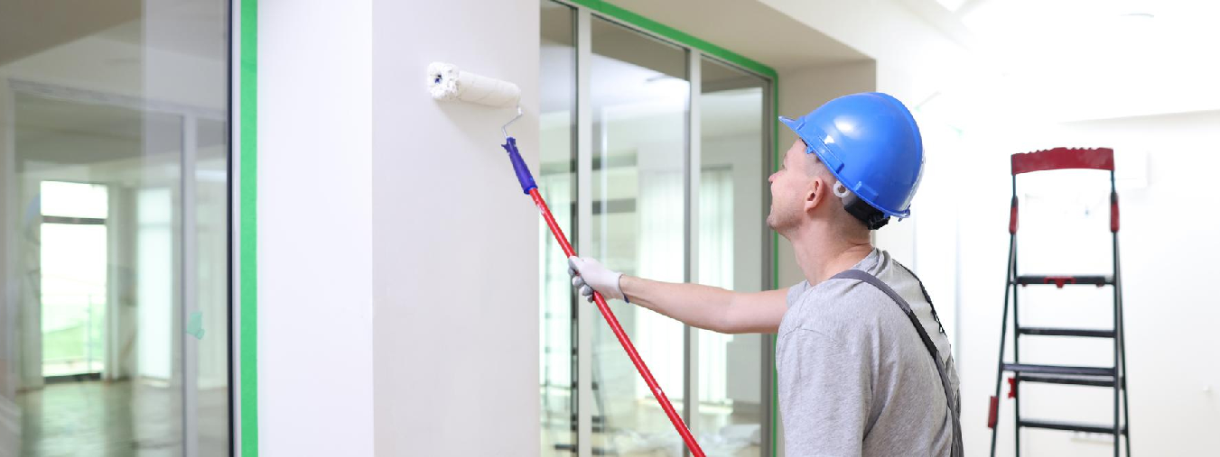 Professional painters in Sarasota applying orange paint on interior wall using rollers and protective suits